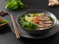 Aromaticzna zupa pho bo z cienko pokrojonym wołowiną, makaronem ryżowym, świeżą miętą, limonką i papryczkami chili.