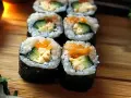 Świeże sushi z awokado, ogórkiem i łososiem, ułożone na drewnianej desce.