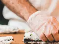 Ręce w rękawiczkach zwijają sushi. Zastanawiasz się, jaka ryba do sushi będzie najlepsza?
