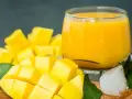 Orzeźwiający mango lassi przepis: pokrojony w kostkę dojrzały mango, szklanka gęstego napoju, kostki lodu i zielone liście.