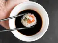 Pałeczki trzymają sushi z łososiem, zanurzając je w miseczce z gęstym słodkim sosem do sushi.