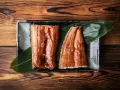 Dwa kawałki błyszczącego, glazurowanego sushi z węgorzem na liściu, podane na czarnej tacce.