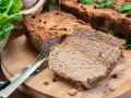 Pyszny pasztet z pieca, pokrojony na plastry, z ziołami i pieprzem. Obok sałata i sztućce.