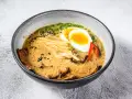 Jak zrobić ramen z zupki chińskiej? Aromatyczny bulion, makaron, jajko na pół, mięso i dodatki w misce.