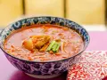 Gorąca zupa z kimchi z kawałkami mięsa i zieloną cebulką, podana w ozdobnej misce.