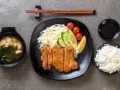 Pyszny schab po japońsku, podany z ryżem, zupą miso, surówką i sosem.