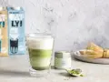 Orzeźwiający iced matcha latte z pianką, obok puszka matcha i bambusowa miotełka. Idealny napój na ciepłe dni.