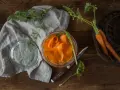 Słoik z marynowaną marchewką do sushi, obok świeże marchewki w koszyku i ściereczka.