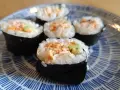 Pięć kawałków sushi z pieczonym łososiem, ryżem i warzywami na niebiesko-białym talerzu.