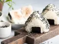 Trójkątne japońskie kulki ryżowe onigiri, posypane czarnym sezamem, z kawałkiem nori.
