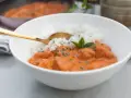 Aksamitny butter chicken masala z ryżem, udekorowany miętą. Złota łyżka zanurzona w daniu.