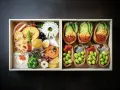 Dwa pudełka z japońskimi przysmakami: jedno z różnorodnymi składnikami, drugie z inari sushi na słodko, wypełnione edamame i ikrą.