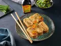 Roladki z omletu do sushi, ozdobione ikrą łososia i szczypiorkiem, obok pałeczki i sosu Maggi.