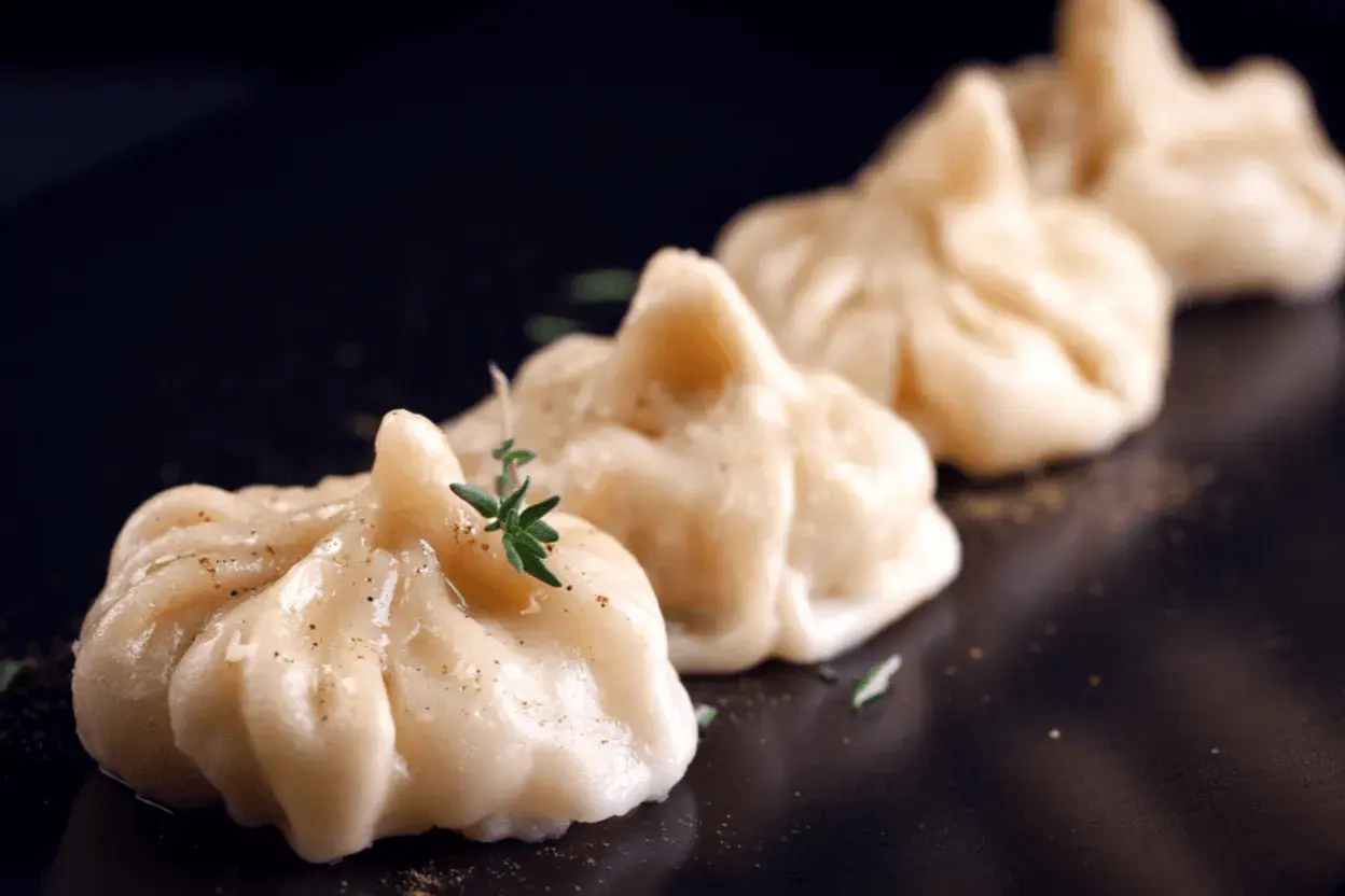 A row of delicate pierożki z krewetkami, garnished with fresh herbs and spices, presented on a dark plate.
