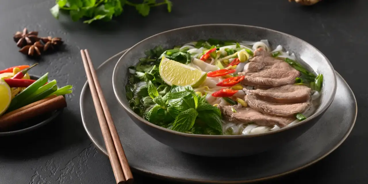 Aromaticzna zupa pho bo z cienko pokrojonym wołowiną, makaronem ryżowym, świeżą miętą, limonką i papryczkami chili.