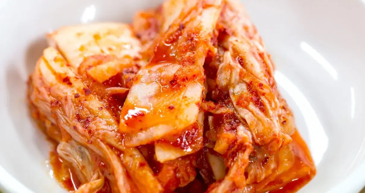 Domowe kimchi w białej misce, z widocznymi liśćmi kapusty i przyprawami.