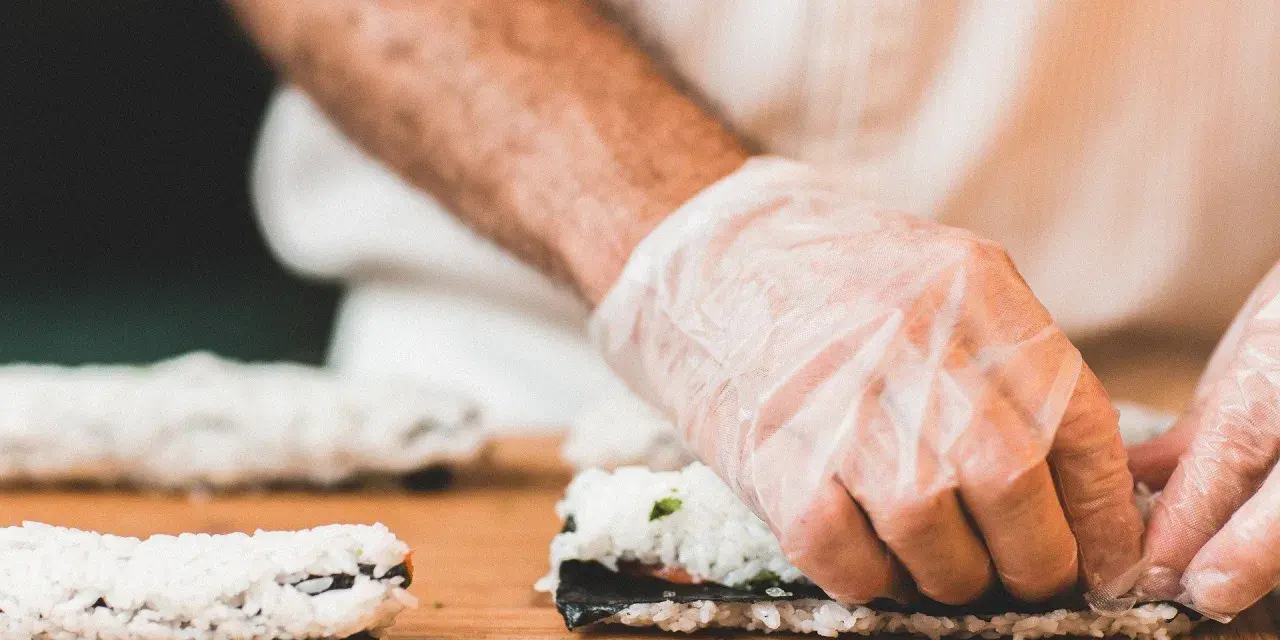 Ręce w rękawiczkach zwijają sushi. Zastanawiasz się, jaka ryba do sushi będzie najlepsza?