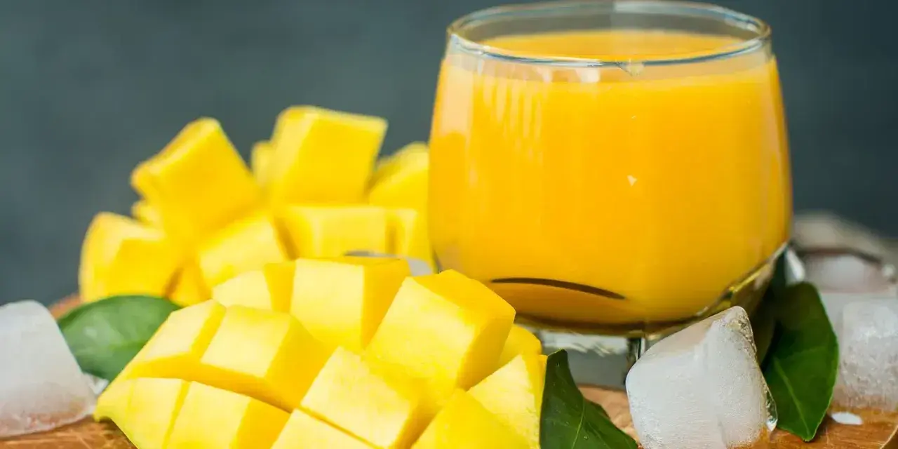 Orzeźwiający mango lassi przepis: pokrojony w kostkę dojrzały mango, szklanka gęstego napoju, kostki lodu i zielone liście.