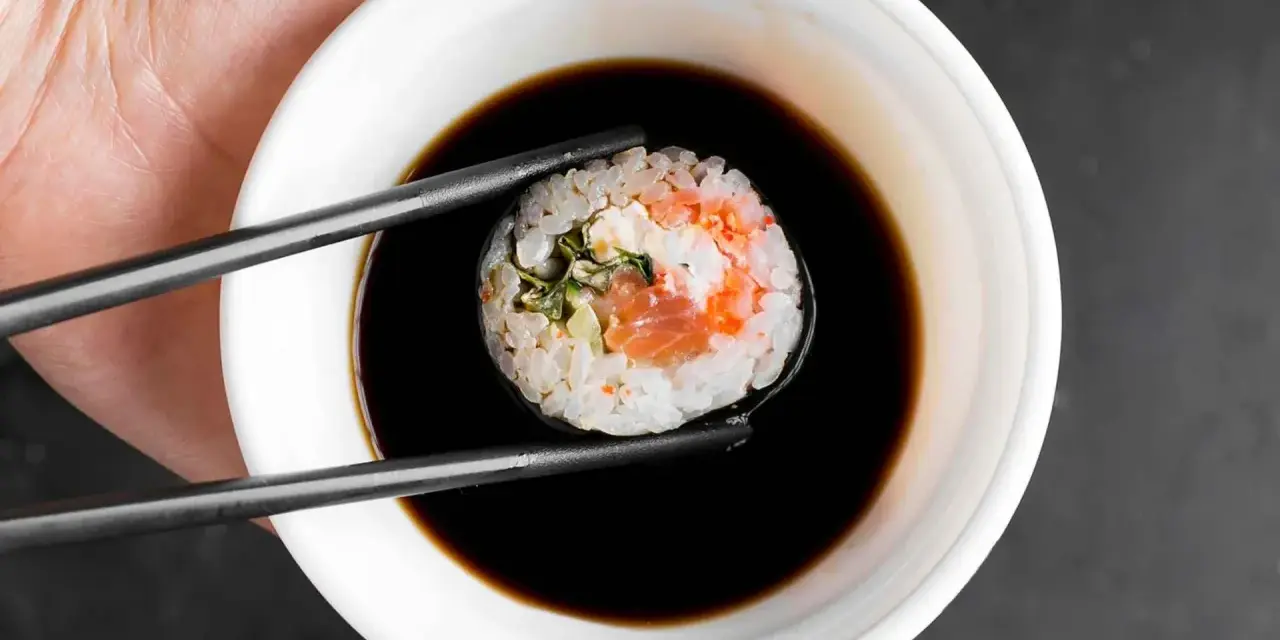 Pałeczki trzymają sushi z łososiem, zanurzając je w miseczce z gęstym słodkim sosem do sushi.