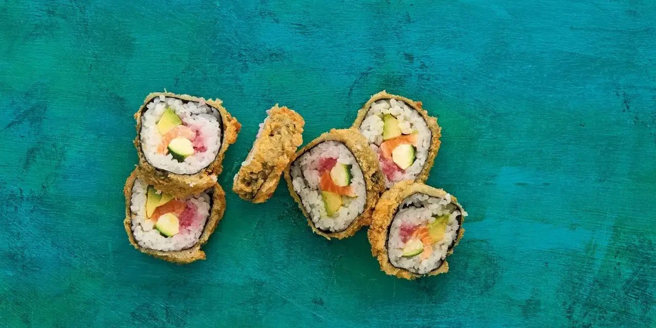 Chrupiące sushi w panko z łososiem, awokado i ogórkiem na turkusowym tle.
