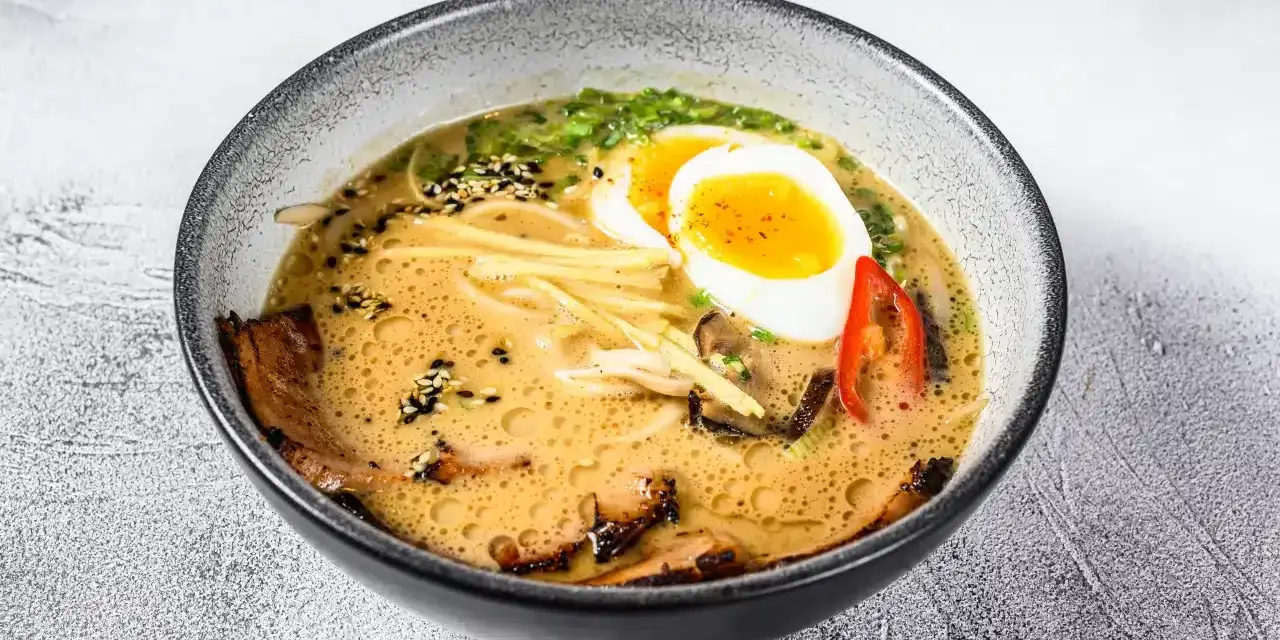 Jak zrobić ramen z zupki chińskiej? Aromatyczny bulion, makaron, jajko na pół, mięso i dodatki w misce.