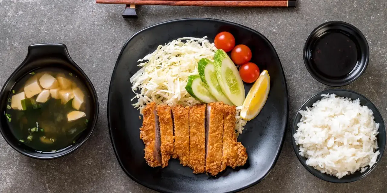 Pyszny schab po japońsku, podany z ryżem, zupą miso, surówką i sosem.