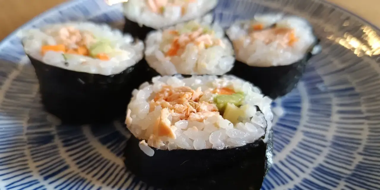 Pięć kawałków sushi z pieczonym łososiem, ryżem i warzywami na niebiesko-białym talerzu.