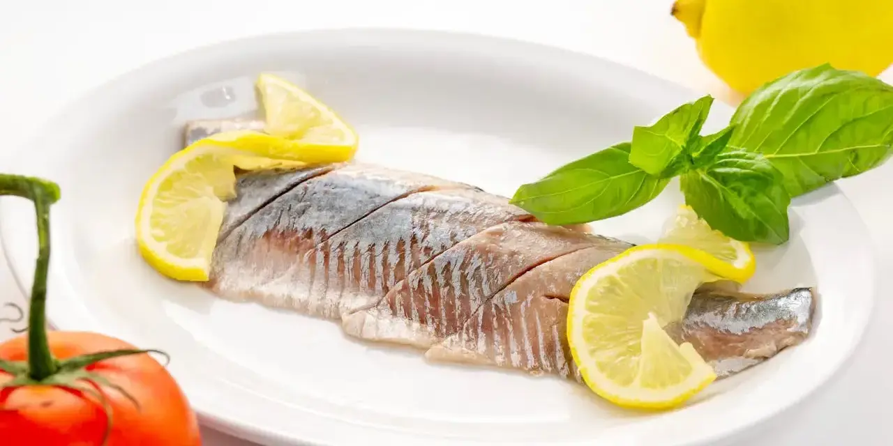 Filety śledzi z cytryną i bazylią na talerzu. Kto nie powinien jeść śledzi? Alergicy i osoby z problemami z cholesterolem.