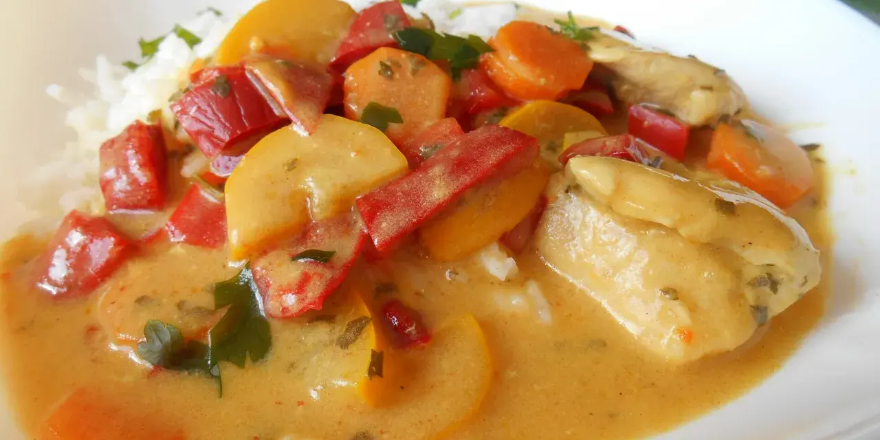 Kurczak curry z warzywami: kawałki kurczaka w kremowym sosie z papryką, marchewką i cukinią, podane z ryżem.