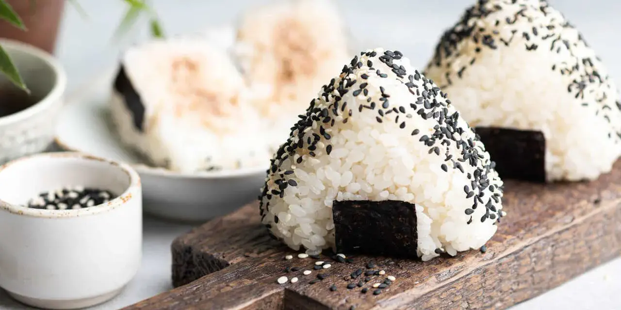 Trójkątne japońskie kulki ryżowe onigiri, posypane czarnym sezamem, z kawałkiem nori.