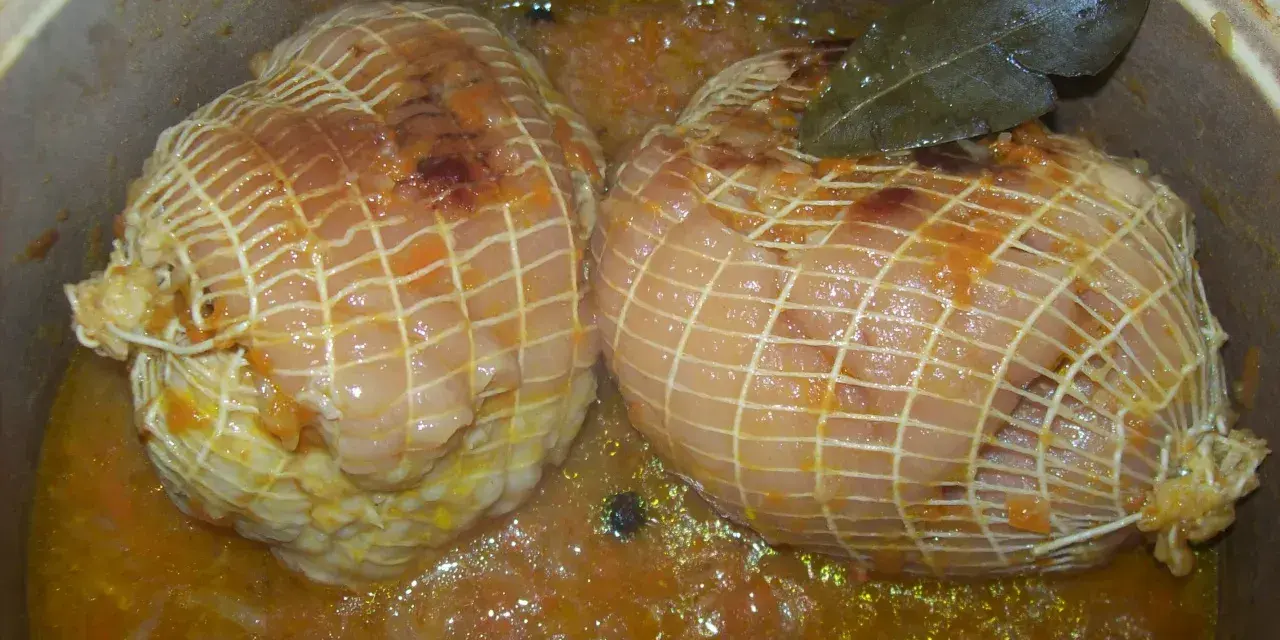 Dwa golonki w siatce, gotujące się w aromatycznym sosie z liściem laurowym. Czas, ile gotować golonki w siatce, zależy od wielkości.