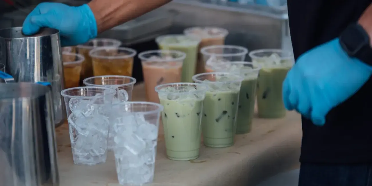 Przygotowanie do zrobienia kulek do bubble tea: ręce w niebieskich rękawiczkach, dzbanki, kubki z lodem i gotowe napoje.