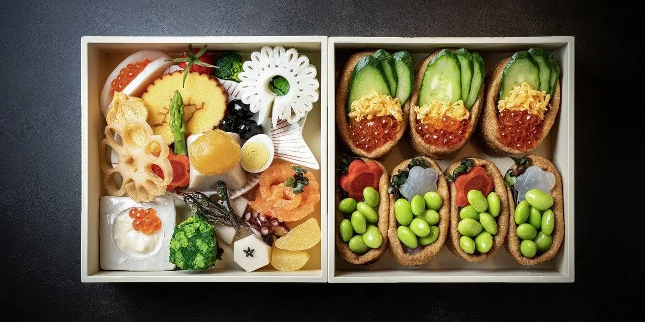 Dwa pudełka z japońskimi przysmakami: jedno z różnorodnymi składnikami, drugie z inari sushi na słodko, wypełnione edamame i ikrą.