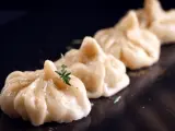 A row of delicate pierożki z krewetkami, garnished with fresh herbs and spices, presented on a dark plate.