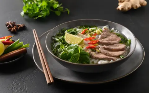 Aromaticzna zupa pho bo z cienko pokrojonym wołowiną, makaronem ryżowym, świeżą miętą, limonką i papryczkami chili.