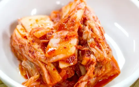 Domowe kimchi w białej misce, z widocznymi liśćmi kapusty i przyprawami.