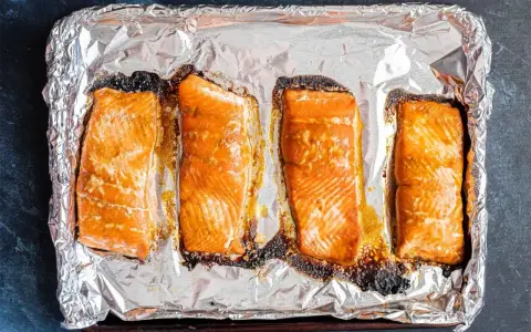 Cztery kawałki łososia pieczone na folii aluminiowej, gotowe do dalszego przygotowania, np. jak przygotować łososia do sushi.
