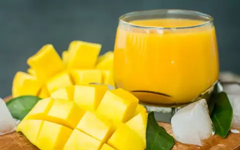 Orzeźwiający mango lassi przepis: pokrojony w kostkę dojrzały mango, szklanka gęstego napoju, kostki lodu i zielone liście.