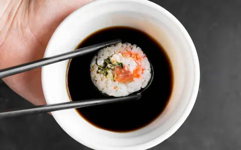 Pałeczki trzymają sushi z łososiem, zanurzając je w miseczce z gęstym słodkim sosem do sushi.