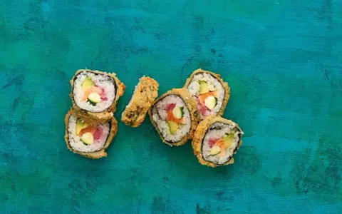 Chrupiące sushi w panko z łososiem, awokado i ogórkiem na turkusowym tle.