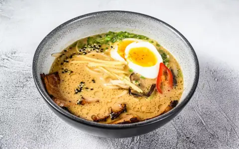 Jak zrobić ramen z zupki chińskiej? Aromatyczny bulion, makaron, jajko na pół, mięso i dodatki w misce.