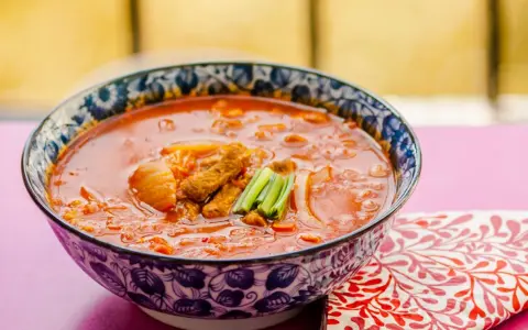 Gorąca zupa z kimchi z kawałkami mięsa i zieloną cebulką, podana w ozdobnej misce.