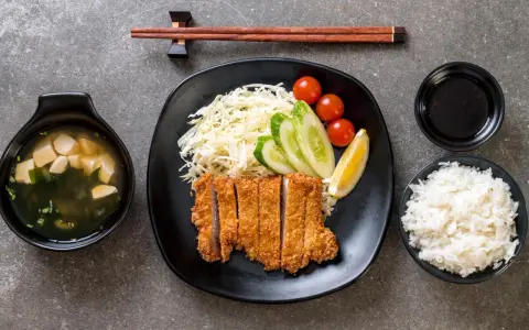 Pyszny schab po japońsku, podany z ryżem, zupą miso, surówką i sosem.