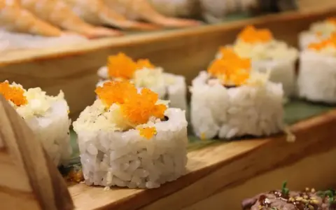 Roladki sushi z pomarańczową ikrą i chrupiącą posypką, idealne do słodkiego sosu do sushi.