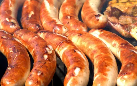 Kilka grubych, rumianych kiełbasek z grilla ułożonych obok siebie.