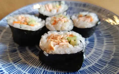 Pięć kawałków sushi z pieczonym łososiem, ryżem i warzywami na niebiesko-białym talerzu.