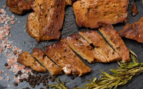 Seitan co to? Pokrojony w plastry, smażony seitan z przyprawami: różową solą, pieprzem i rozmarynem.