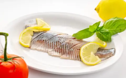 Filety śledzi z cytryną i bazylią na talerzu. Kto nie powinien jeść śledzi? Alergicy i osoby z problemami z cholesterolem.