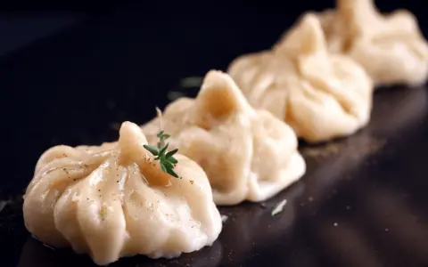A row of delicate pierożki z krewetkami, garnished with fresh herbs and spices, presented on a dark plate.