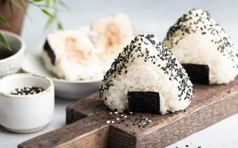Trójkątne japońskie kulki ryżowe onigiri, posypane czarnym sezamem, z kawałkiem nori.